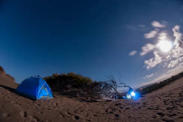 Descriptive scene of the night sky with the Milky Way during the eclipse of the moon on January 21, 2019, where the very dark skies are clearly seen on the sand dunes of Bani in the Dominican Republic. A blue tent enhances the interest of the composition where all the elements draw attention to venturing into adventure tourism