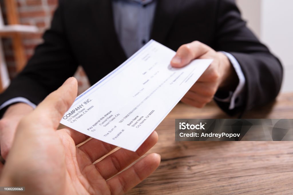 Man's Hands Giving Cheque To Other Person Close-up Of Businessman's Hands Giving Cheque To Other Person In Office Check - Financial Item Stock Photo