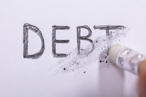 Close-up Of Pencil Eraser Erasing Debt Word On White Paper