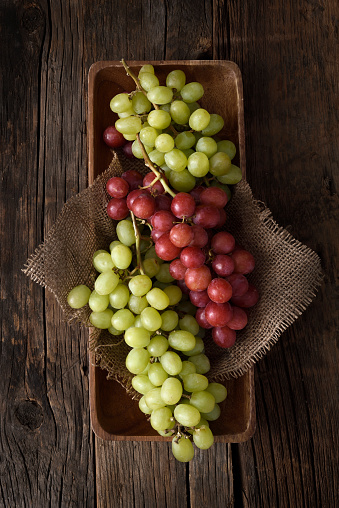 Fresh bunch of red and white grapes in a wooden on a dark wooden background