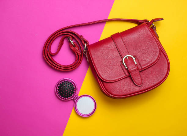 Red leather bag and mini-mirror comb on a colored paper background. Top view, minimalism.