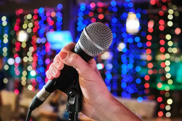 Photo of Microphone in man hands close-up on an abstract bokeh background. Blurred background with lights