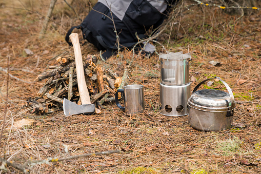 axe near a firewoods, camping woodstove, camping utensils and backpack on the background
