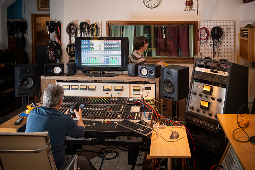 Musician with cables and engineer at mixing console preparing to record in analog to digital studio.  Vancouver, British Columbia, Canada