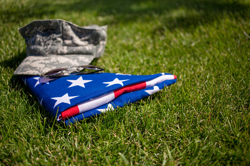 Carefully folded United States flag and military cap on green grass