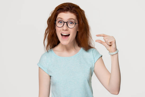 istock Funny excited redhead woman showing something tiny isolated on background 1130250099