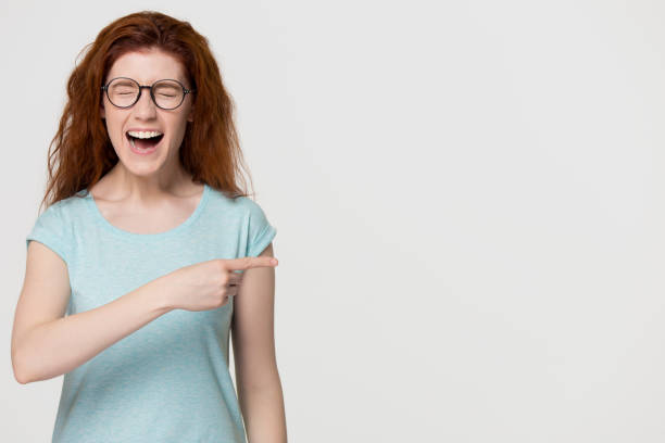 Cheerful red-haired woman laughing pointing at funny advertisement copy space Cheerful red-haired woman laughing out loud pointing finger at funny advertisement copy space aside, happy overjoyed redhead girl screaming with joy laughter isolated on white grey studio background child laughing hysterically stock pictures, royalty-free photos & images