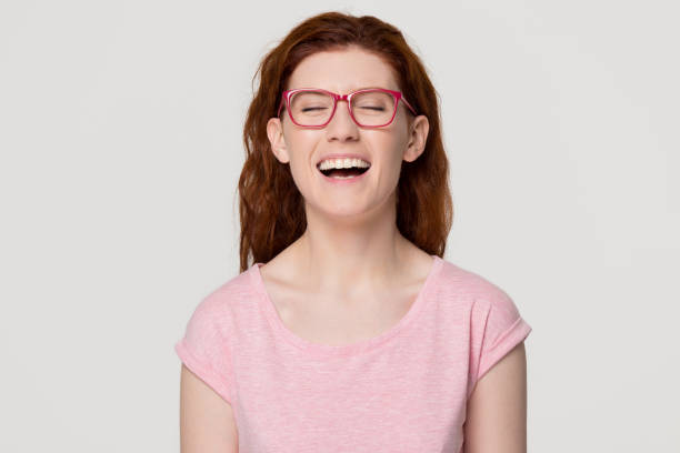 Happy funny redhead girl laughing out loud at humorous joke Happy funny redhead girl in pink glasses laughing out loud at humorous joke, cheerful young red-haired woman screaming with positive emotions laughter isolated on white grey blank studio background child laughing hysterically stock pictures, royalty-free photos & images