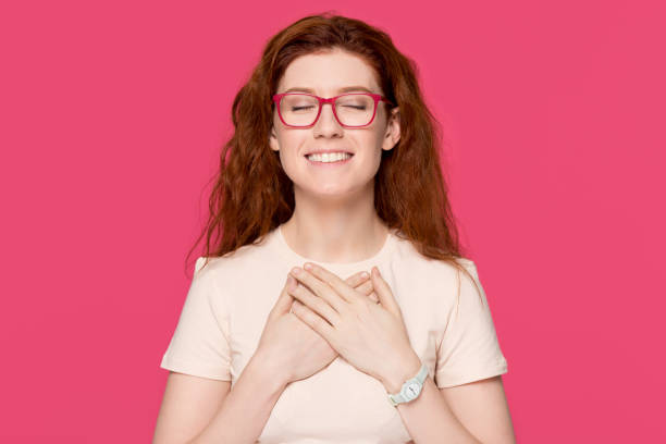 Happy grateful red-haired woman holding hands on chest feel appreciation