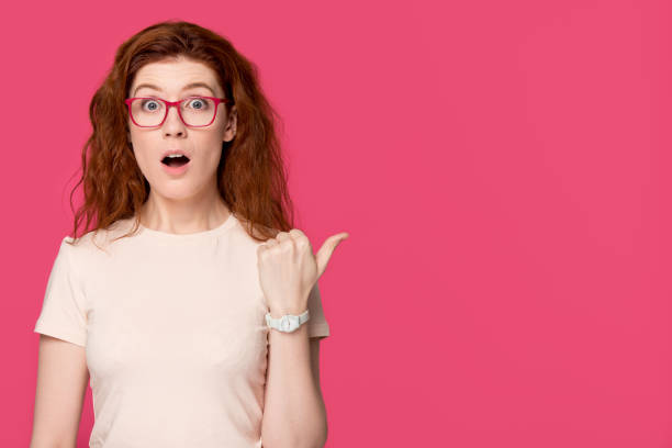 istock Shocked amazed redhead girl in glasses pointing aside at copyspace 1130250153