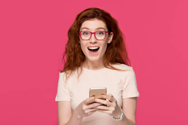 istock Excited redhead woman holding cell phone amazed by mobile win 1130250163