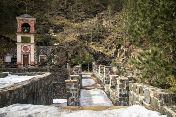 istock Small church by the river and stone bridge on fast river with small waterfall 1130254174