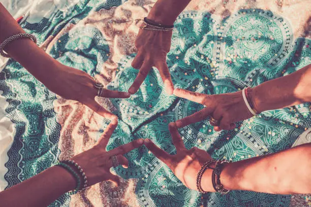 Photo of Close up with above top view of group of women hands together doing the V like victory sign - team crew work and friendship concept - blue mandala textile background on the flor