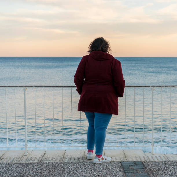 istock Young fat woman standing alone on the beach 1130257735