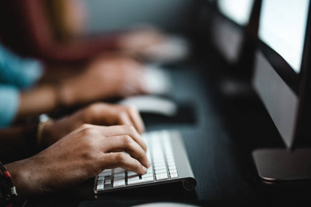 Close up of unrecognizable man typing e-mail on desktop PC. Close up of unrecognizable male student typing on keyboard while using desktop PC at school. computer lab stock pictures, royalty-free photos & images