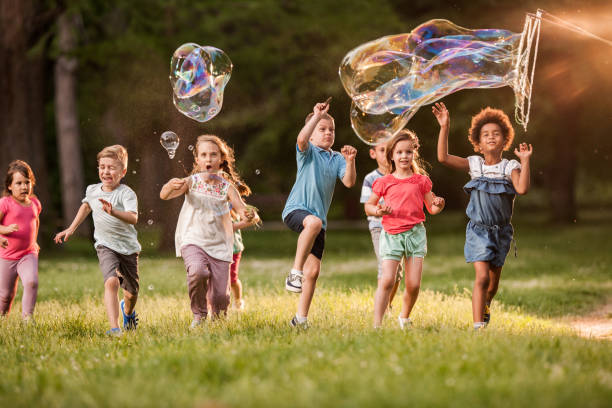 Carefree kids having fun while running and splashing rainbow bubbles in the park.