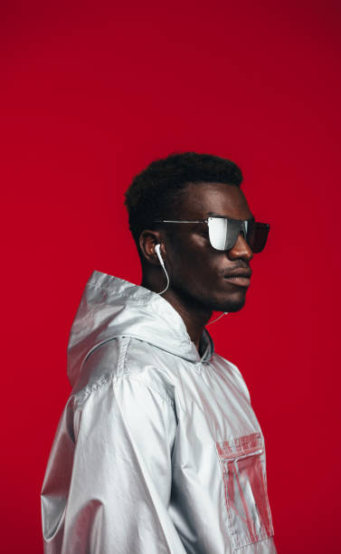 African man in futuristic style clothing African man in futuristic outfit against red background. Man in stylish sunglasses,  silver hoodie and earphones. fashion model men male sunglasses stock pictures, royalty-free photos & images