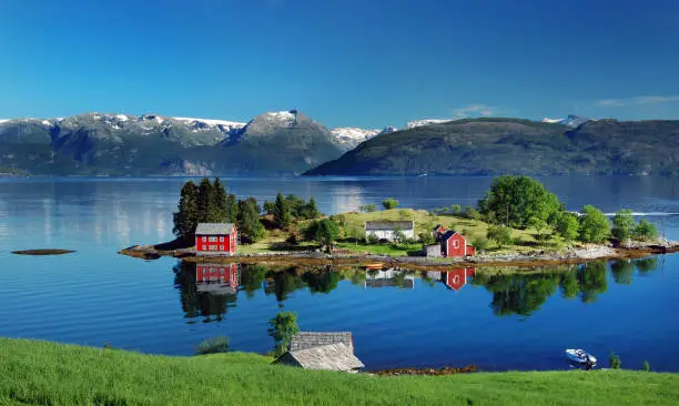 Hardangerfjord in south western Norway in the summer. A red, Norwegian house situated on a small island in the fjord. In the distance the Folgefonna glacier. Photo was taken near the village of Omastranda.