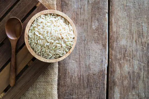 Photo of raw brown whole grain semi-milled rice in wood bowl