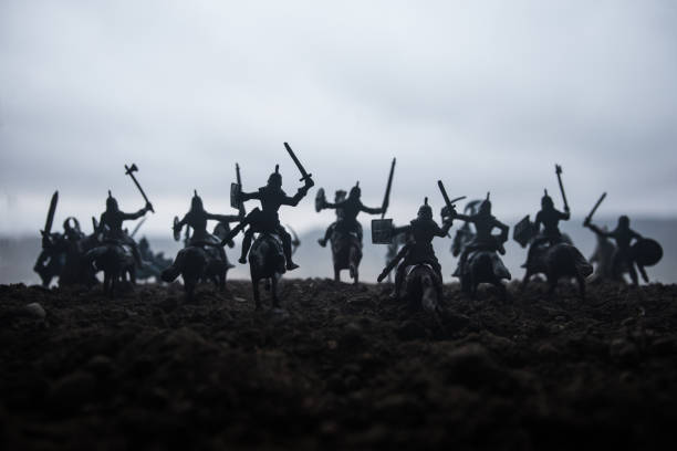 istock Medieval battle scene with cavalry and infantry. Silhouettes of figures as separate objects, fight between warriors on sunset foggy background. Selective focus 1130283907