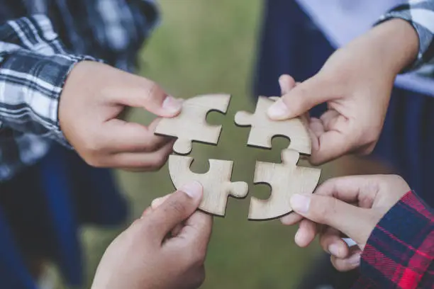 Photo of people helping in assembling puzzle, cooperation in decision making, team support in solving problems and corporate group teamwork concept, close up view of hands connecting pieces