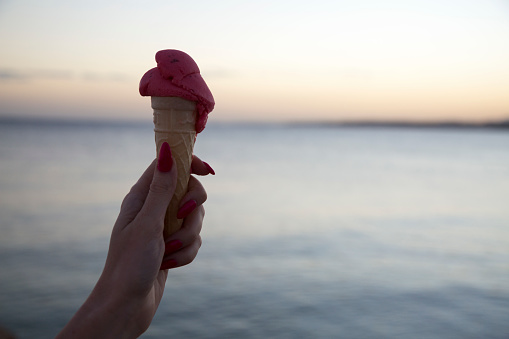 Female hand holding ice cream cone in front of sea