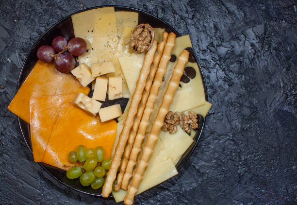 istock Cheese plate on a black background: Lambert, Cheddar, Gouda, breadsticks on a slate with space for text. Tasty snack. The view from the top. Copy space. 1130292018