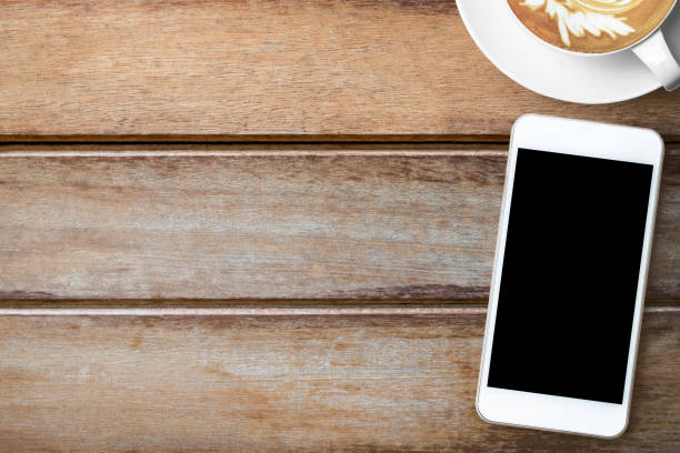 istock Smartphone with black blank screen is on top of wood table with coffee cup. Top view with copy space, flat lay. Coffee shop mobile application concept. 1130295648