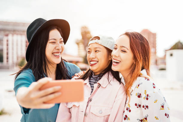 携帯電話スマート フォン屋外 - 新しい技術アプリケーション - 人々、社会、友情、技術、若者ライフ スタイル コンセプトを楽しんで若いトレンディなティーンエイ ジャーと selfie を取って� - 日本　スペイン ストックフォトと画像