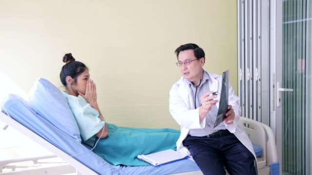 Doctor showing X-ray film to patient with illness in hospital room with sadness