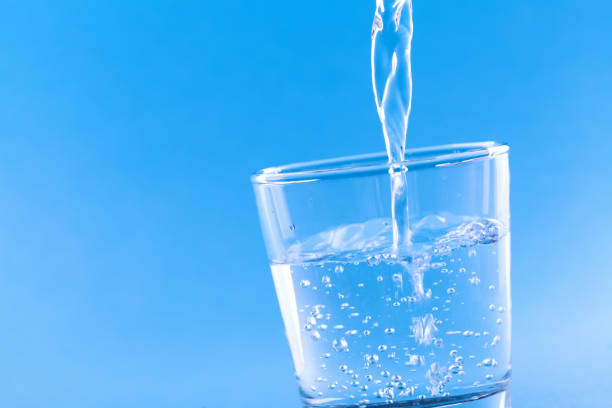 istock Drinking water pouring into glass against blue background. 1130306036