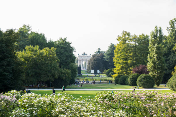 people walking on the parco sempione, the large public park in milano city, italy. in the background the arch of peace. - milan italy italy castello sforzesco color image imagens e fotografias de stock