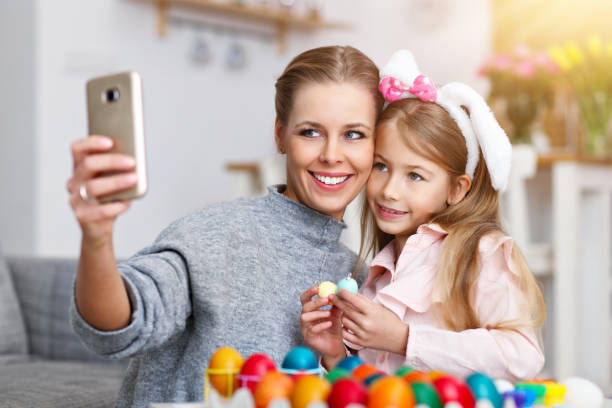 istock Mother and daughter painting Easter eggs and taking selfie 1130308701