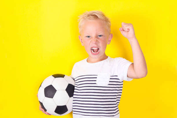 istock Cute blond boy portrait with ball on yellow background 1130309299