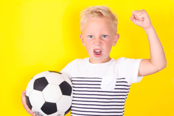istock Cute blond boy portrait with ball on yellow background 1130309340