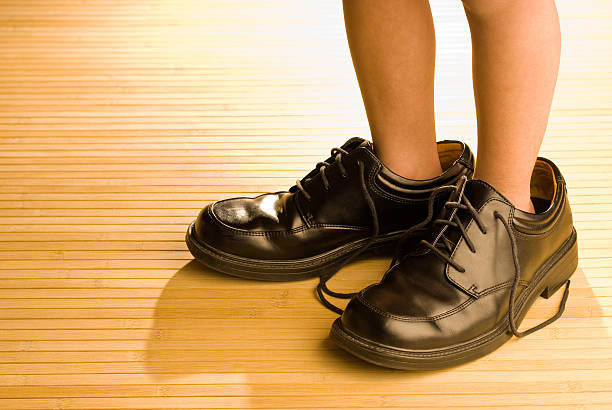 big chaussures à remplir, enfant pieds dans les chaussures noires - trop grand photos et images de collection