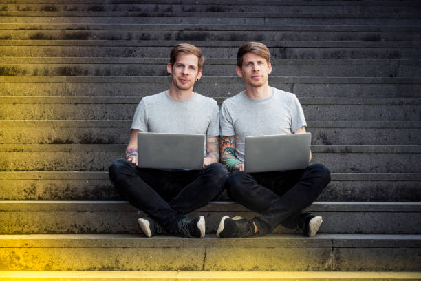 twin brothers with laptops sitting on stairs twin brothers with laptops sitting on stairs in urban surounding, free wifi. two men same clothes stock pictures, royalty-free photos & images