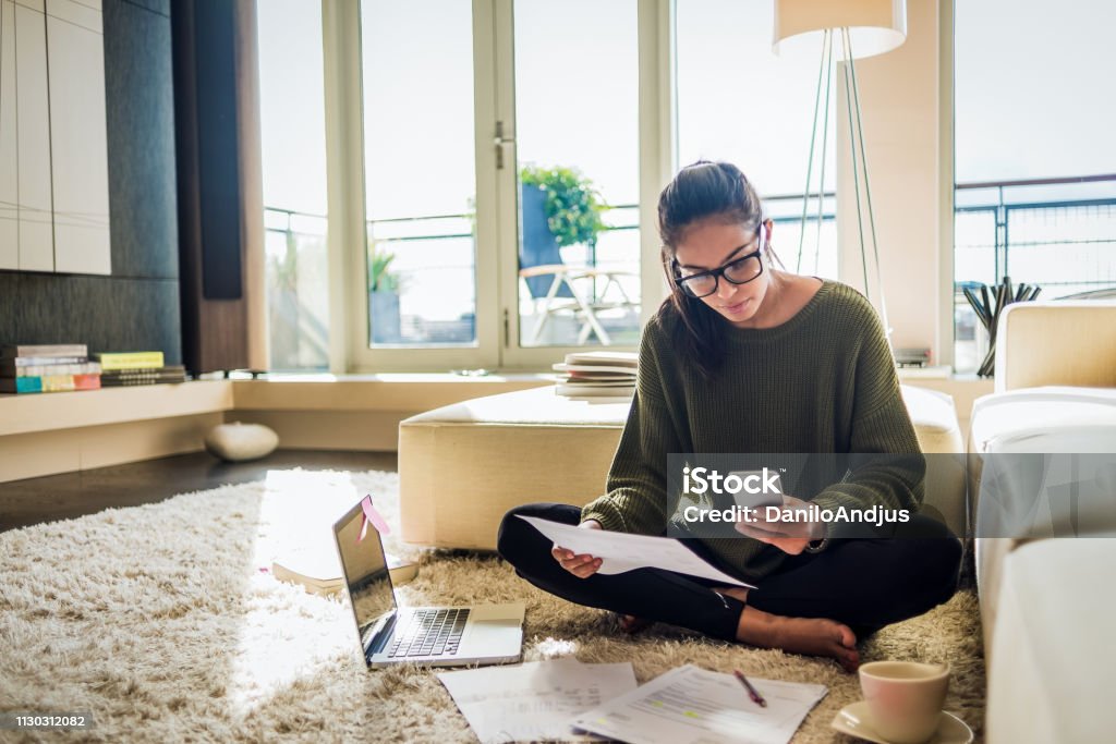 young woman working from home young woman sitting on the floor of her living room and working Financial Bill Stock Photo
