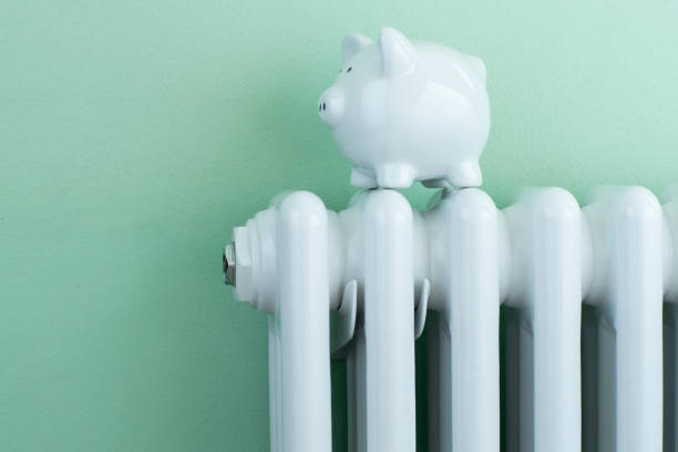 piggy bank balanced on radiator to illustrate energy costs - power saving imagens e fotografias de stock