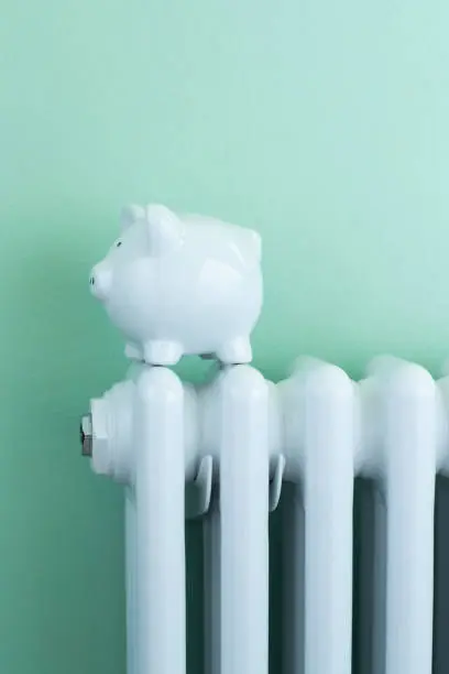 Photo of Piggy Bank Balanced On Radiator To Illustrate Energy Costs