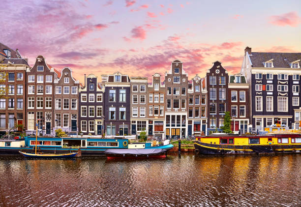 Amsterdam, Netherlands. Houseboats, dancing houses Amsterdam, Netherlands. Floating Houses and houseboats and boats at channels by banks. Traditional dutch dancing houses among trees. Evening autumn street above water pink sunset sky with clouds. houseboat photos stock pictures, royalty-free photos & images