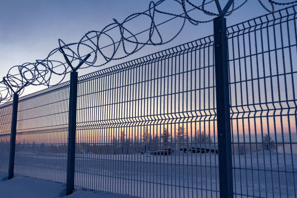 clôture avec fil barbelé à la frontière de l'objet à l'aube en hiver. norilsk - winter wire barbed wire protection photos et images de collection