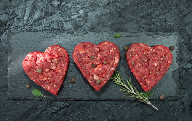 patty di carne macinata a forma di cuore per un hamburger con condimenti su uno sfondo nero vista dall'alto - meat beef love heart shape foto e immagini stock
