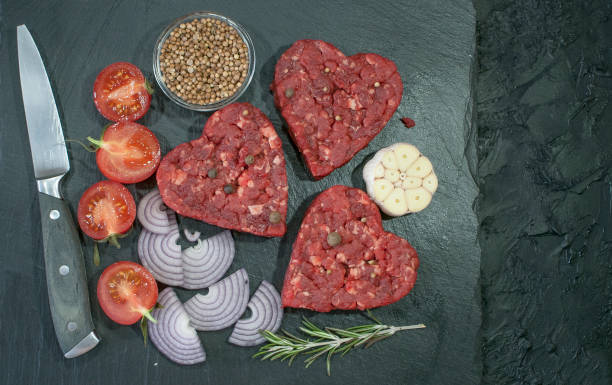 patty di carne macinata a forma di cuore per un hamburger con condimenti su uno sfondo nero. spazio di copia - meat beef love heart shape foto e immagini stock