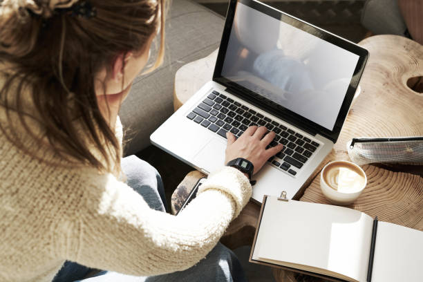 istock Woman's working on laptop, screen space for design layout. Having coffee at modern cafe, on wooden slab table, sunshine. 1130336530