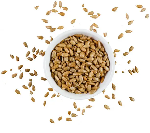 Heap of peeled and roasted sunflower seeds in a bowl on white background shot directly from above