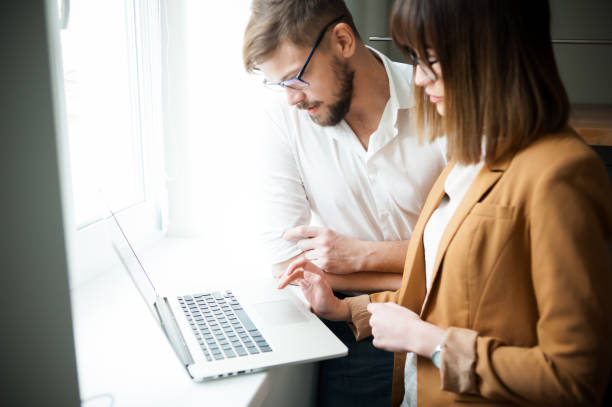 istock Two young coworkers dressed casual using laptop in white interior 1130343977