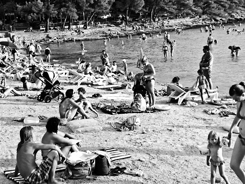 Beautiful outdoors in black and white: Families and tourists enjoying a sunny day tanning and swimming on the beachside of the Adriatic sea, Croatia