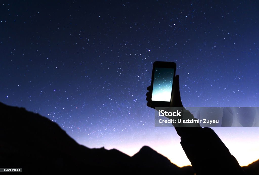 A hand is holding smartphone with starry sky photo: a man is taking a photo starry sky at night. Milky way and galaxy on dark sky. Wifi mobile internet concept Star - Space Stock Photo