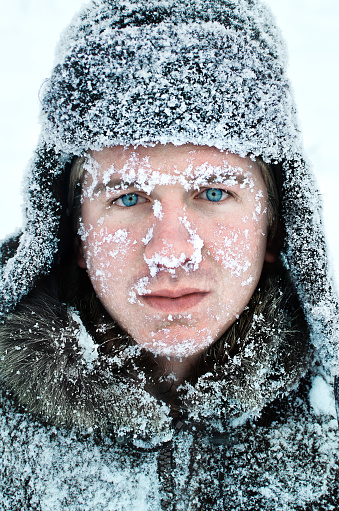 male face covered with snow with bright blue eyes